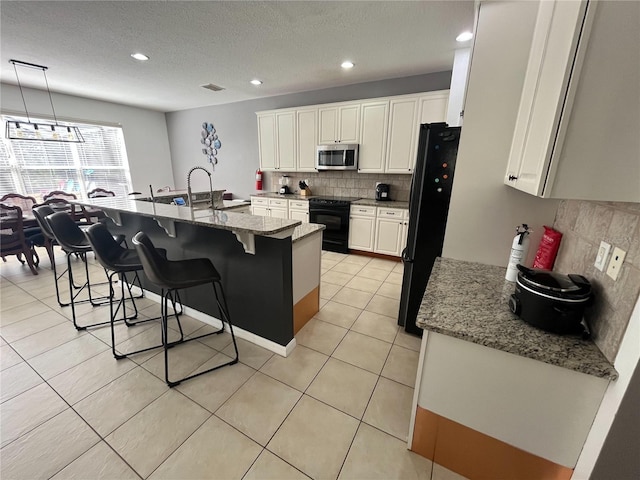 kitchen with a breakfast bar area, white cabinets, light tile patterned flooring, and black appliances