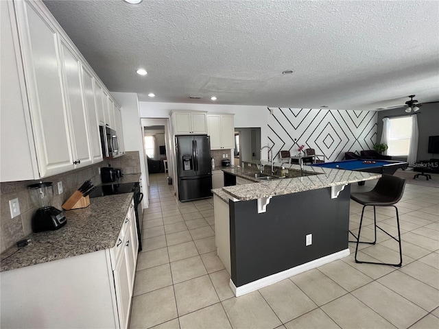 kitchen featuring light tile patterned floors, white cabinets, a sink, black appliances, and a kitchen breakfast bar