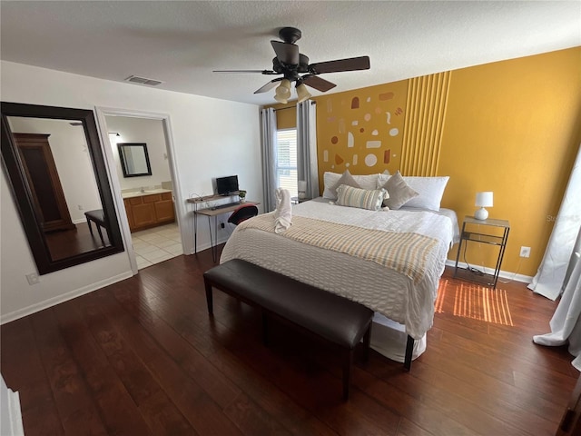 bedroom featuring visible vents, baseboards, hardwood / wood-style floors, ensuite bathroom, and a textured ceiling