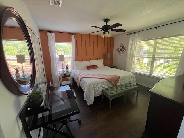 bedroom featuring ceiling fan, a textured ceiling, visible vents, baseboards, and dark wood-style floors