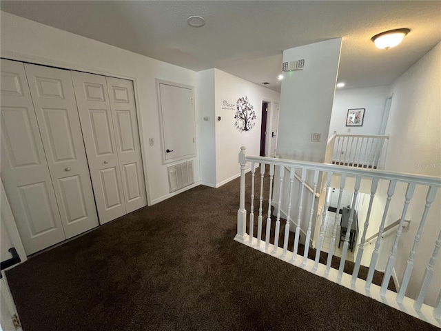 hallway with carpet, visible vents, baseboards, and an upstairs landing