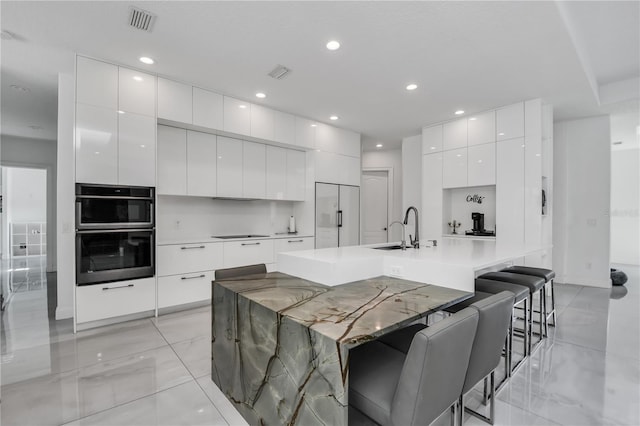 kitchen featuring built in refrigerator, double oven, white cabinets, a kitchen bar, and a large island with sink