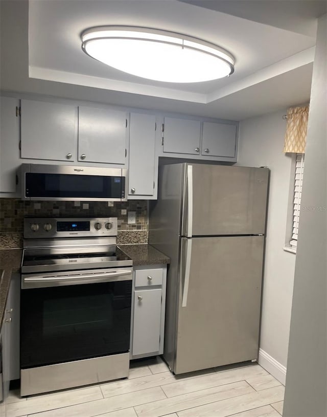 kitchen with dark countertops, wood tiled floor, a tray ceiling, gray cabinets, and stainless steel appliances