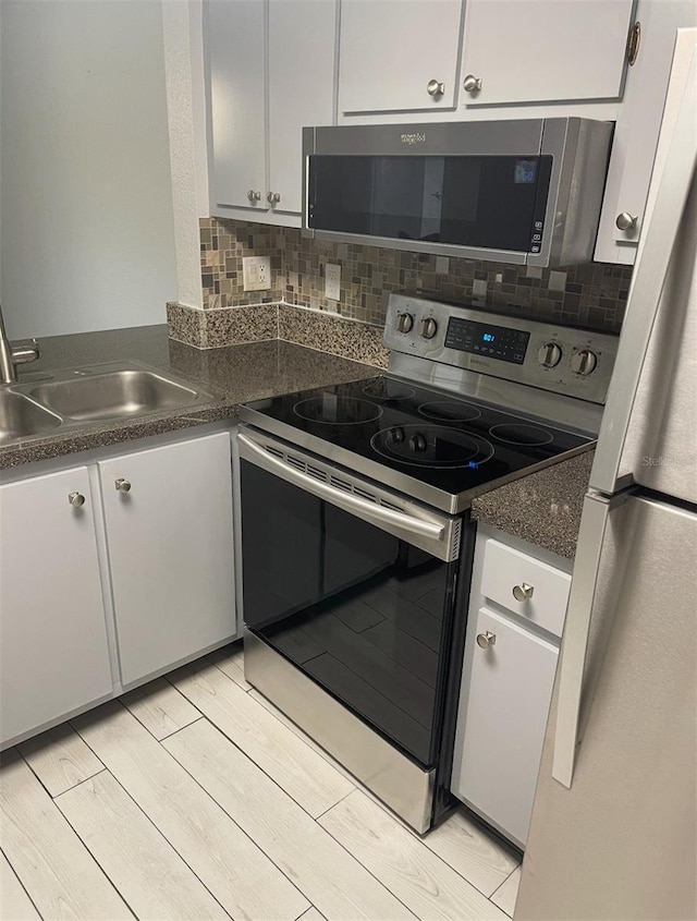 kitchen with stainless steel appliances, dark countertops, backsplash, light wood-style flooring, and a sink