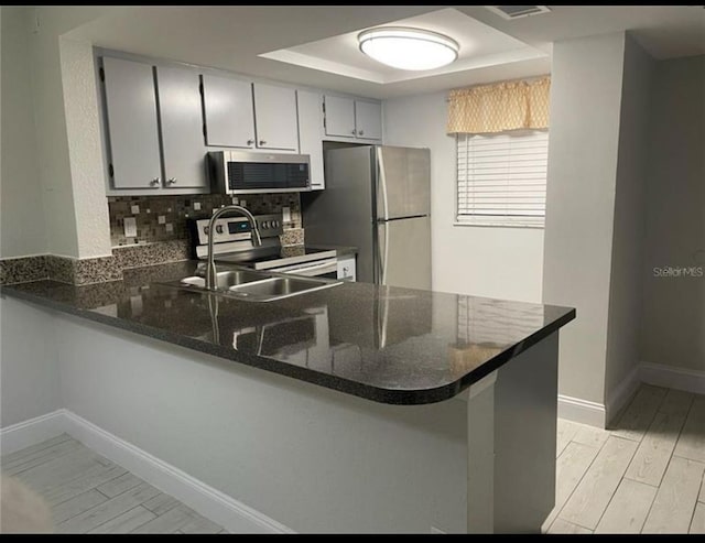 kitchen with a tray ceiling, wood finish floors, appliances with stainless steel finishes, a sink, and a peninsula