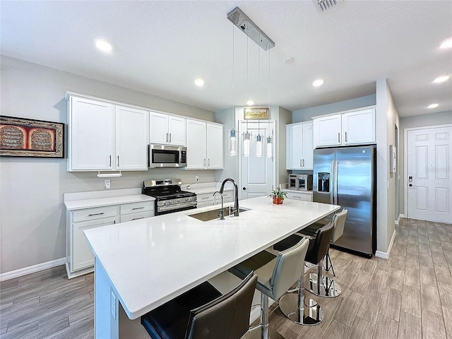 kitchen with appliances with stainless steel finishes, pendant lighting, an island with sink, sink, and white cabinets