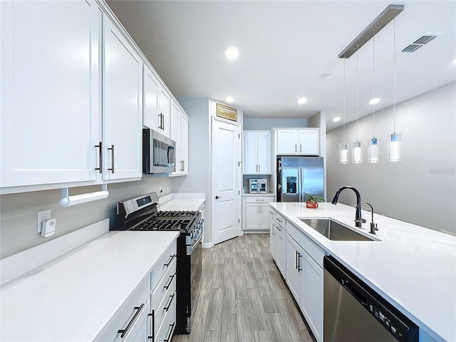 kitchen featuring pendant lighting, white cabinetry, sink, stainless steel appliances, and light hardwood / wood-style flooring