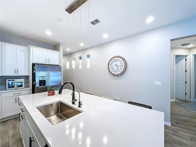 kitchen featuring white cabinetry, stainless steel fridge, sink, and hanging light fixtures