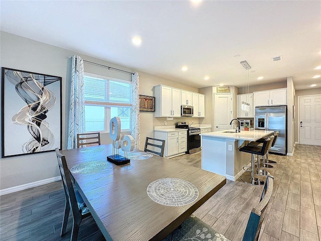 kitchen with sink, white cabinetry, hanging light fixtures, a center island with sink, and appliances with stainless steel finishes