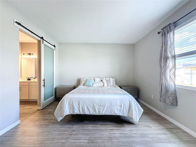 bedroom featuring a barn door, connected bathroom, a textured ceiling, and light wood-type flooring