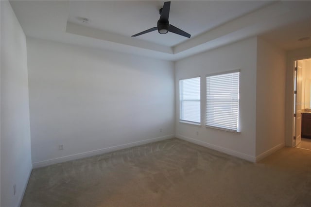 spare room with ceiling fan, a tray ceiling, and carpet