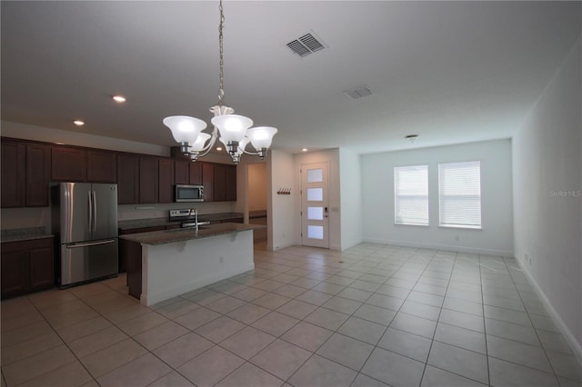 kitchen featuring sink, hanging light fixtures, appliances with stainless steel finishes, dark stone counters, and a kitchen island with sink