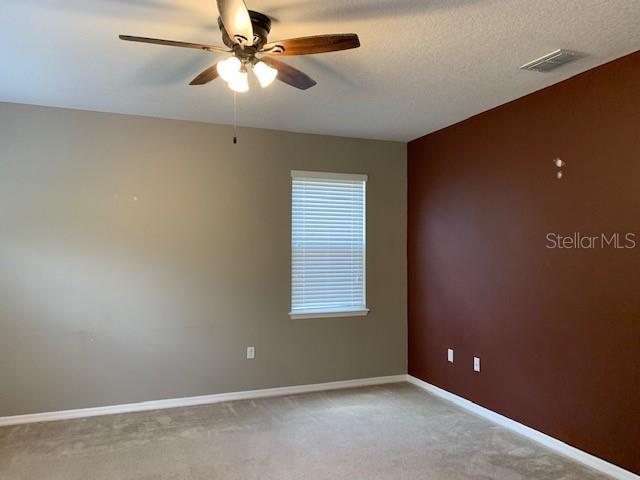 unfurnished room featuring visible vents, a textured ceiling, baseboards, light colored carpet, and ceiling fan