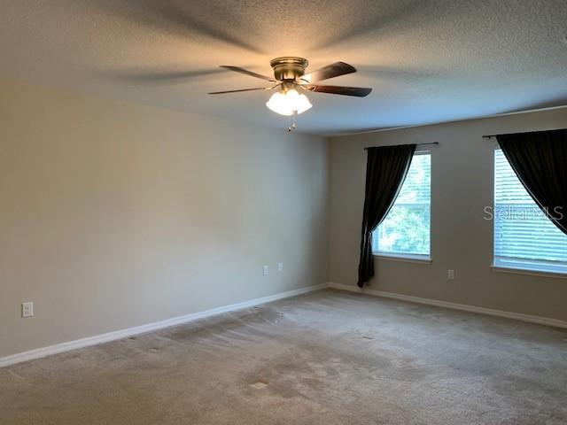 spare room with light colored carpet, a textured ceiling, a ceiling fan, and baseboards