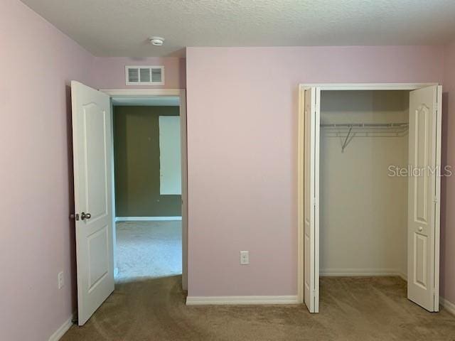 unfurnished bedroom featuring visible vents, a textured ceiling, a closet, carpet flooring, and baseboards