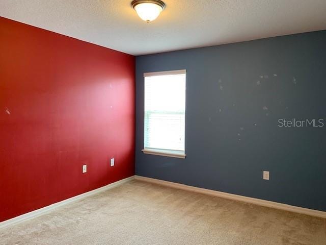 empty room with a textured ceiling, baseboards, and carpet