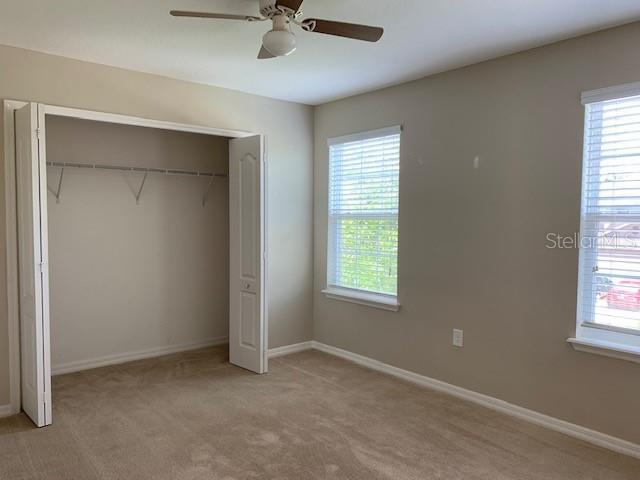 unfurnished bedroom featuring a closet, light carpet, baseboards, and a ceiling fan