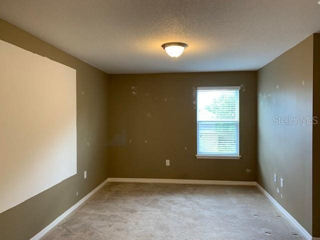 carpeted spare room featuring a textured ceiling and baseboards