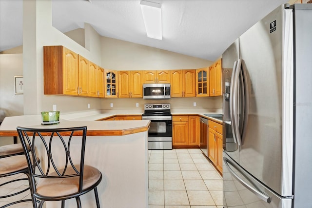 kitchen featuring light tile patterned flooring, vaulted ceiling, a kitchen breakfast bar, kitchen peninsula, and stainless steel appliances