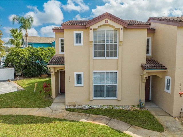 mediterranean / spanish-style house with a tile roof, a front lawn, and stucco siding