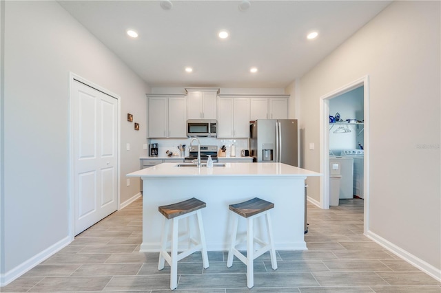 kitchen with a center island with sink, stainless steel appliances, light countertops, a sink, and independent washer and dryer