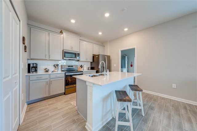 kitchen featuring sink, gray cabinetry, stainless steel appliances, a center island with sink, and decorative backsplash