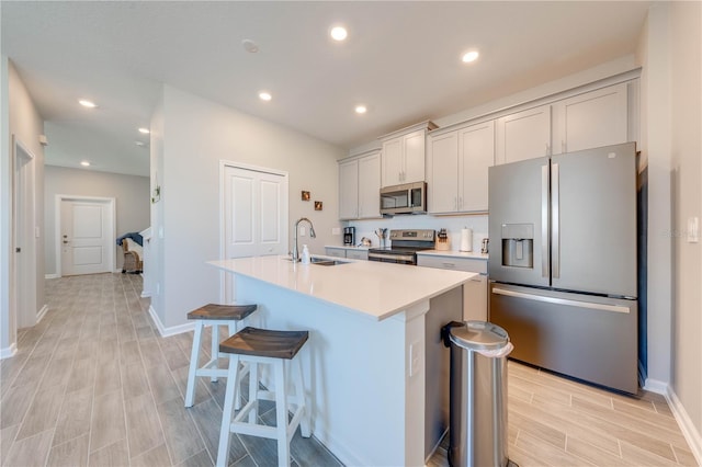 kitchen featuring a sink, light countertops, appliances with stainless steel finishes, gray cabinets, and an island with sink