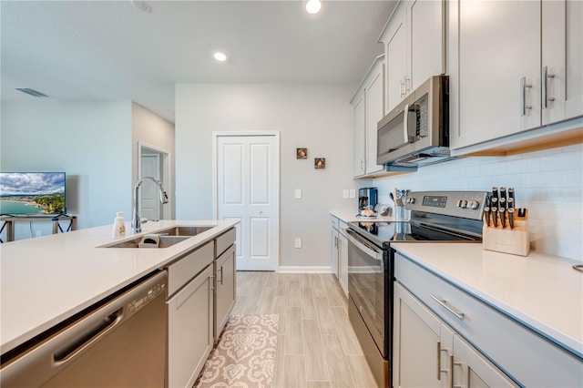 kitchen with tasteful backsplash, appliances with stainless steel finishes, sink, and light wood-type flooring