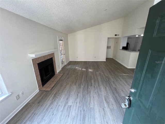 unfurnished living room featuring lofted ceiling, dark hardwood / wood-style floors, a tiled fireplace, and a textured ceiling