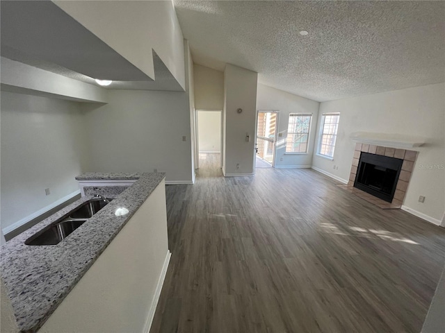 unfurnished living room with lofted ceiling, sink, a textured ceiling, dark hardwood / wood-style flooring, and a tiled fireplace