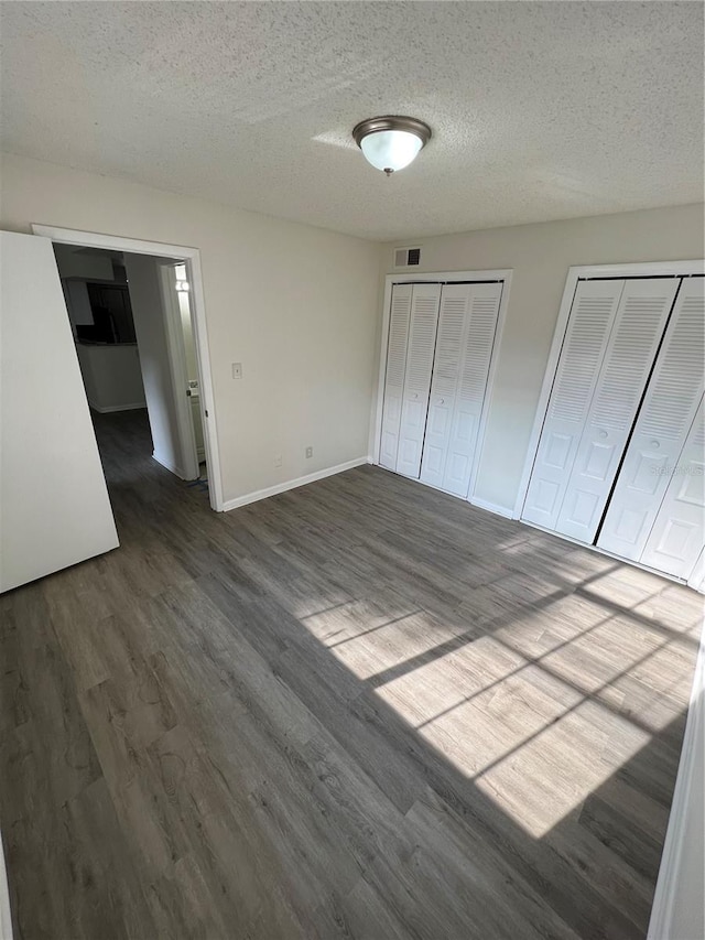 unfurnished bedroom with dark hardwood / wood-style floors, two closets, and a textured ceiling