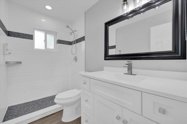 bathroom featuring tiled shower, vanity, toilet, and wood-type flooring