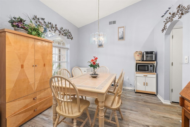 dining room featuring hardwood / wood-style flooring, lofted ceiling, and a notable chandelier