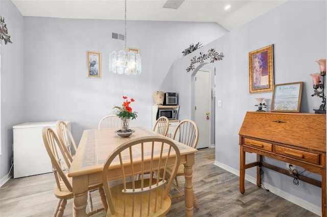 dining space with a notable chandelier, lofted ceiling, and light wood-type flooring