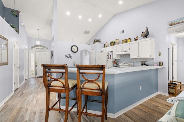 kitchen with white cabinetry, a kitchen bar, white fridge with ice dispenser, light hardwood / wood-style floors, and kitchen peninsula