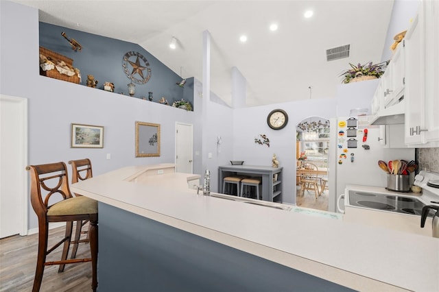 kitchen featuring a kitchen bar, electric range oven, kitchen peninsula, hardwood / wood-style flooring, and white cabinets