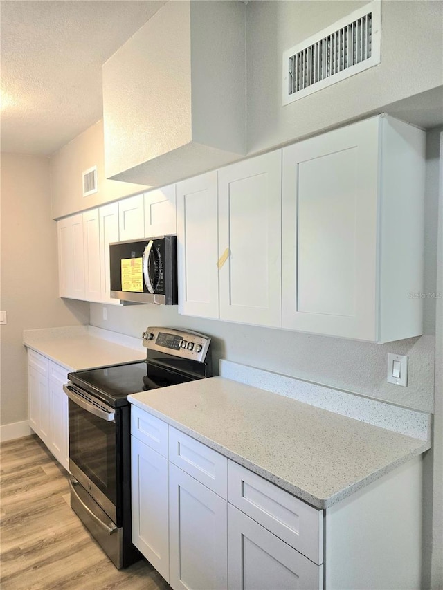 kitchen featuring light stone counters, white cabinetry, a textured ceiling, light hardwood / wood-style floors, and stainless steel appliances