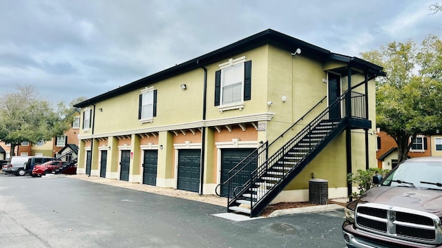 view of front facade featuring community garages, stairway, central AC unit, and stucco siding