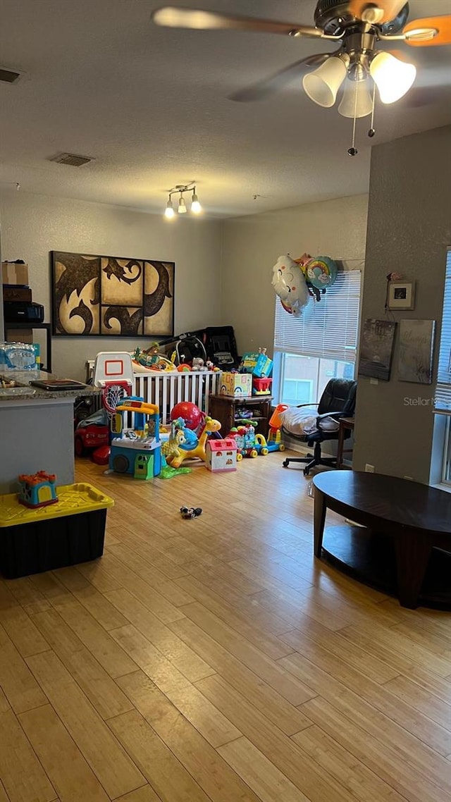 recreation room with ceiling fan, wood finished floors, and visible vents