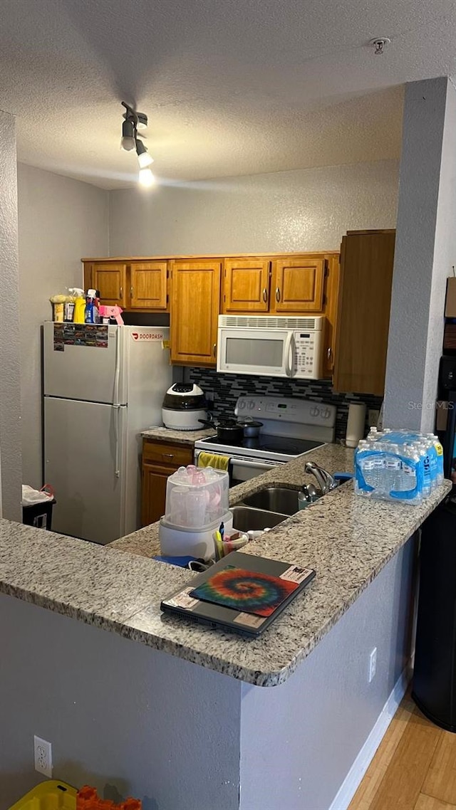 kitchen featuring brown cabinets, decorative backsplash, light wood-type flooring, white appliances, and a peninsula