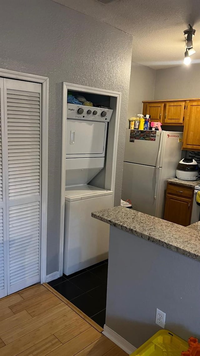 kitchen featuring stacked washer and dryer, a textured wall, brown cabinetry, freestanding refrigerator, and wood finished floors