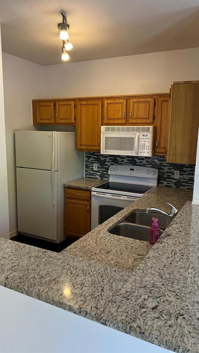 kitchen with a sink, backsplash, brown cabinetry, and white appliances