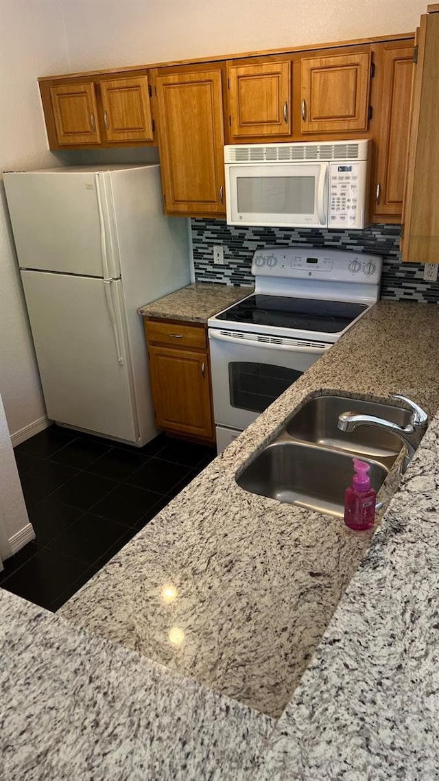 kitchen with white appliances, tasteful backsplash, a sink, and brown cabinetry