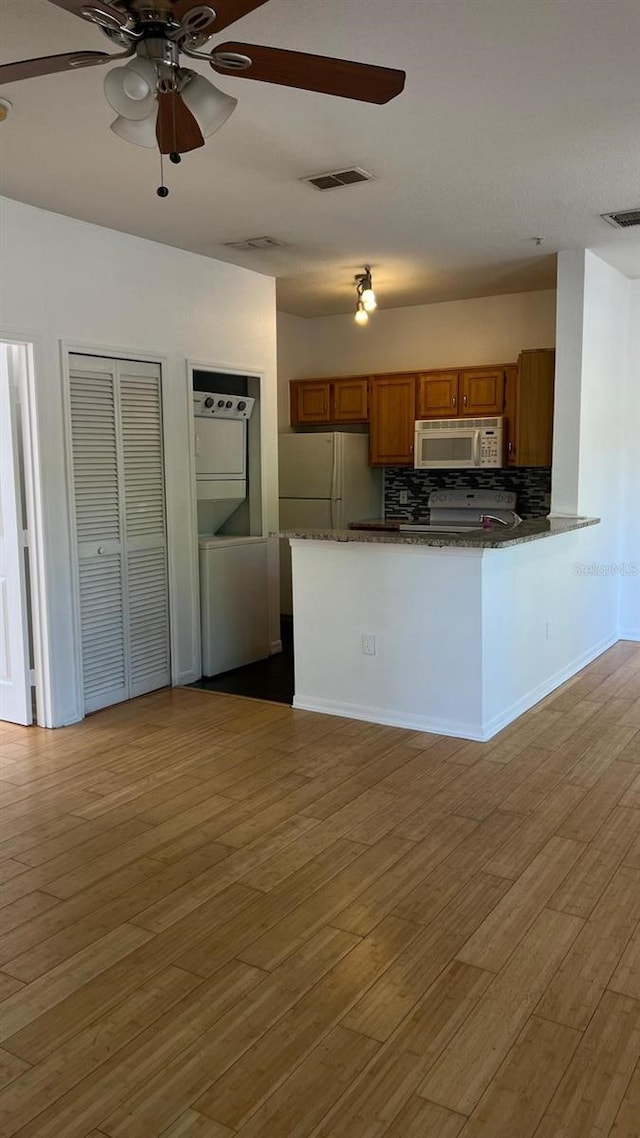 kitchen with stacked washer and dryer, light wood finished floors, brown cabinets, white appliances, and ceiling fan