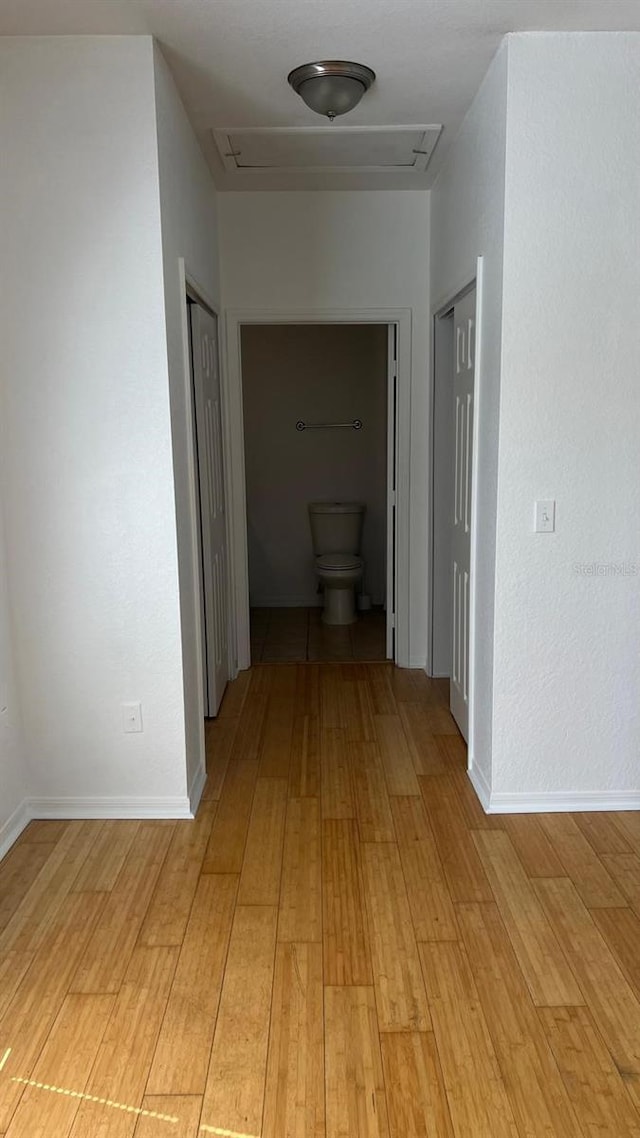 hall with attic access, baseboards, and light wood-type flooring
