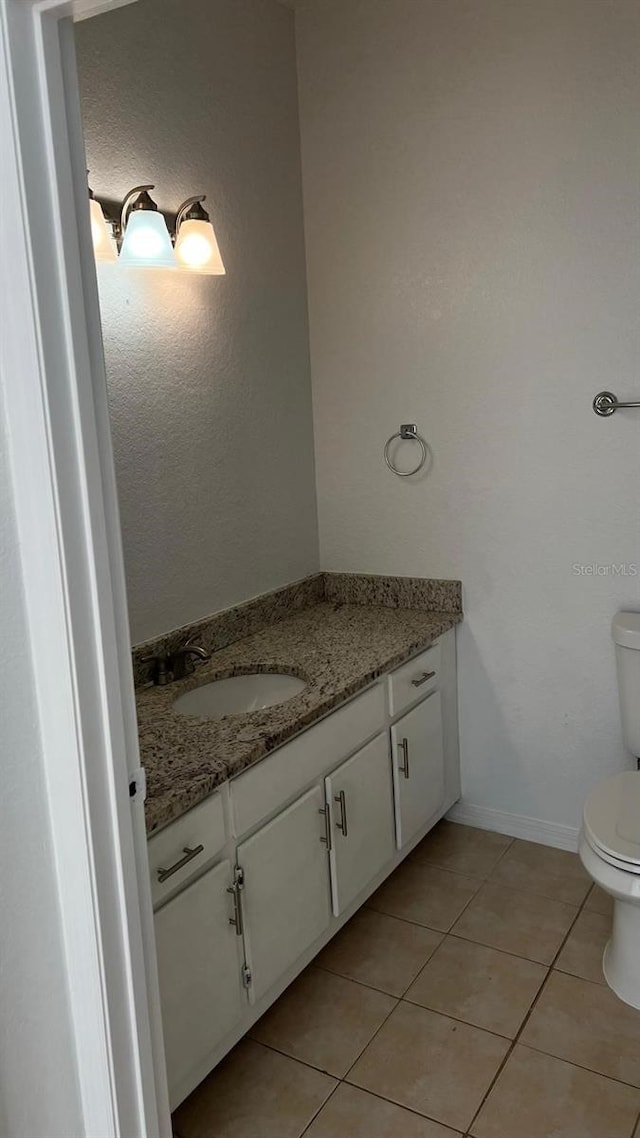 half bathroom with toilet, vanity, tile patterned floors, and baseboards
