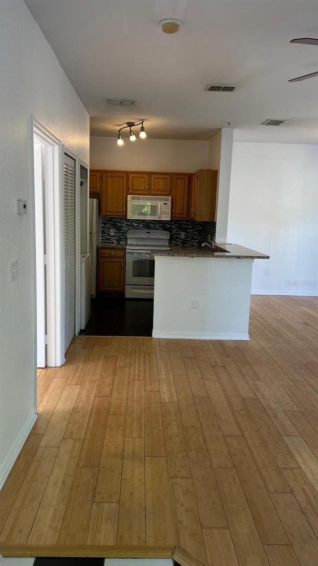 kitchen with backsplash, dark countertops, brown cabinets, and white appliances