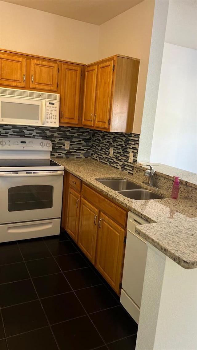 kitchen featuring brown cabinetry, a sink, backsplash, and white appliances
