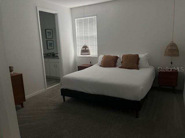 bedroom with dark colored carpet, ensuite bath, and baseboards