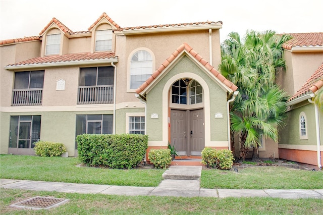 view of front of home with a tile roof, a front yard, and stucco siding